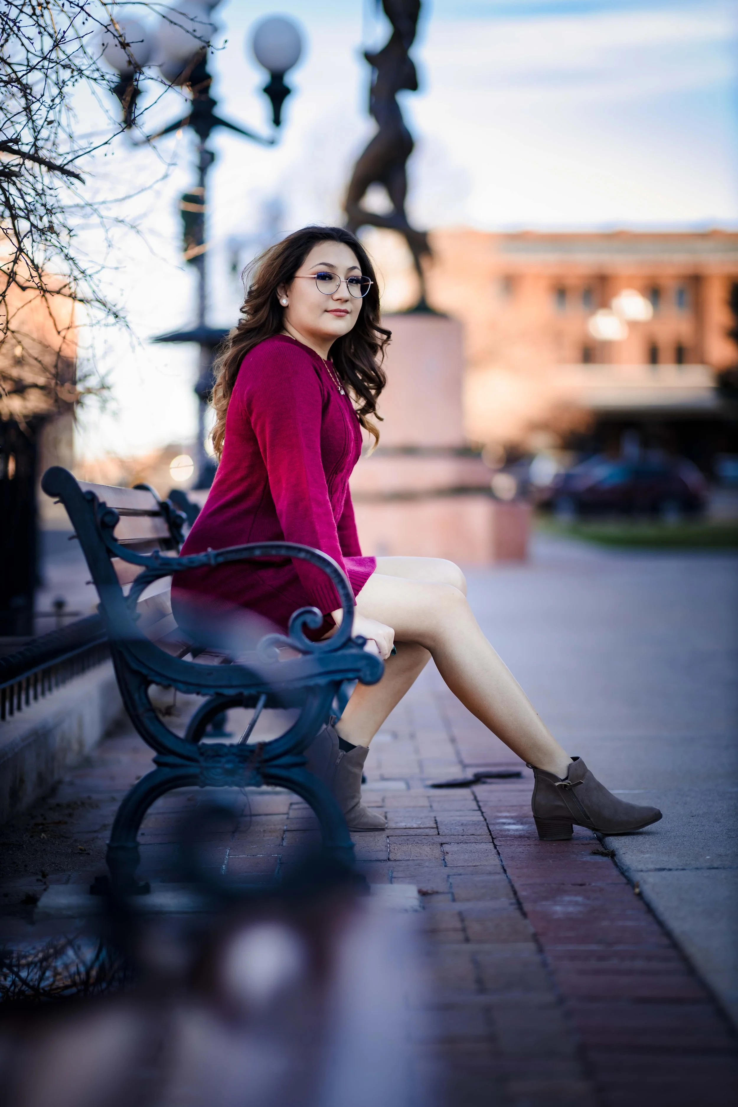 A woman and a young girl are smiling and hugging outdoors near a body of water during autumn, with colorful fall trees in the background.