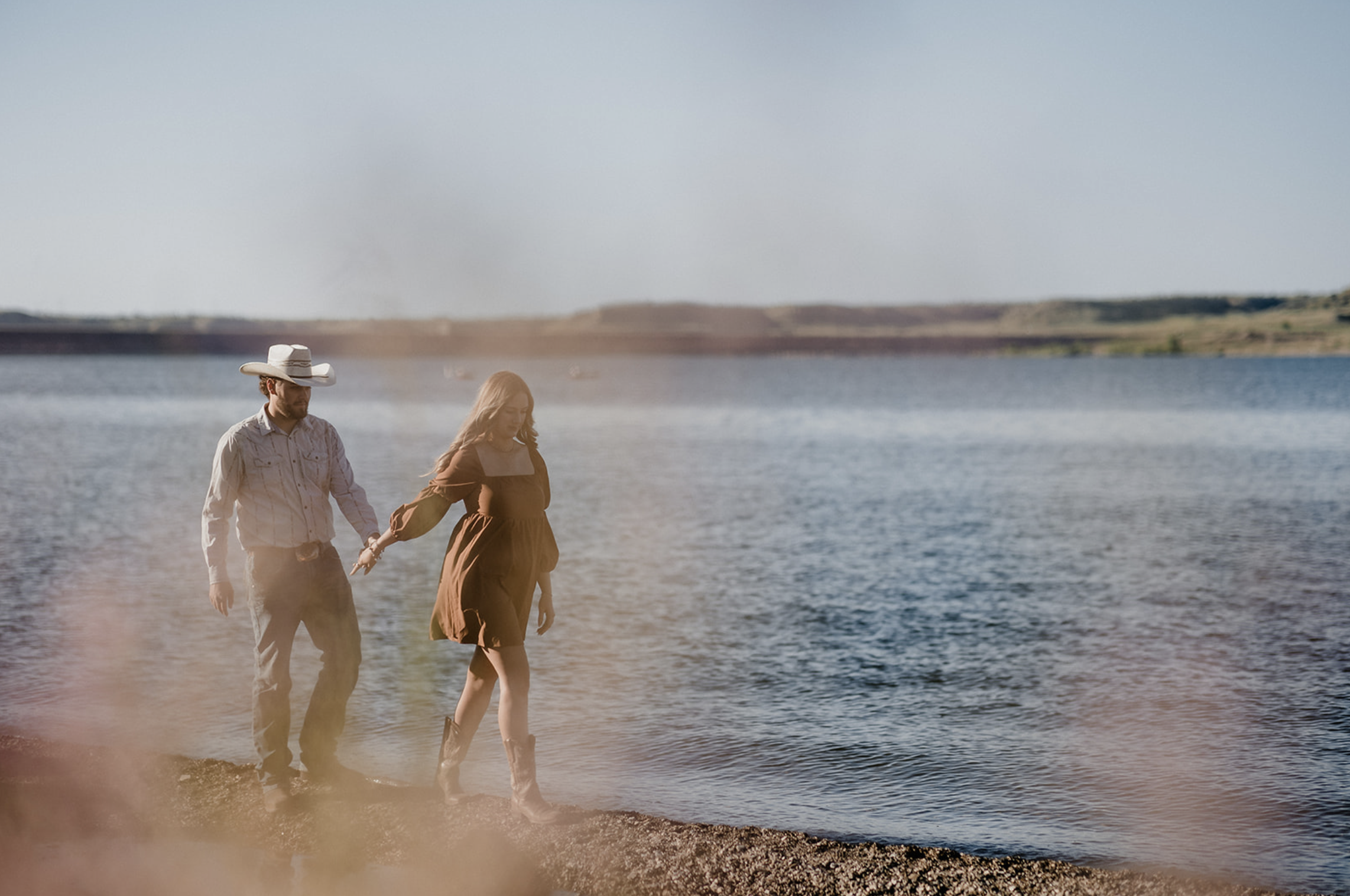 Young man sitting outdoors on grass near a tree, wearing a colorful floral shirt and blue jeans, with a thoughtful expression.