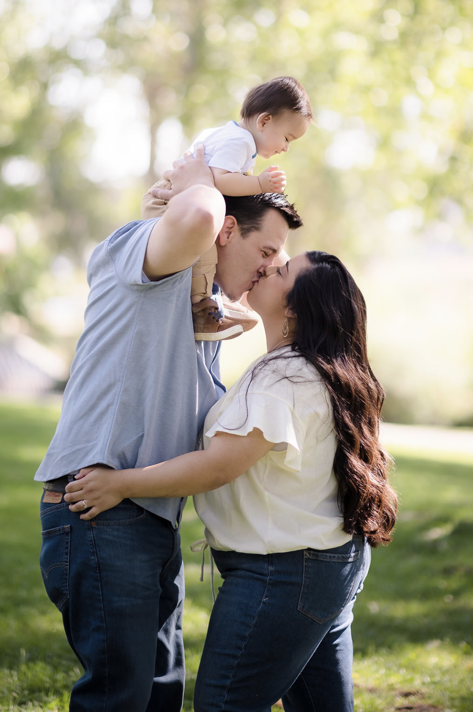 A young woman with curly brown hair, wearing a white dress, sitting on a fallen tree trunk in a lush green forest, smiling at the camera.