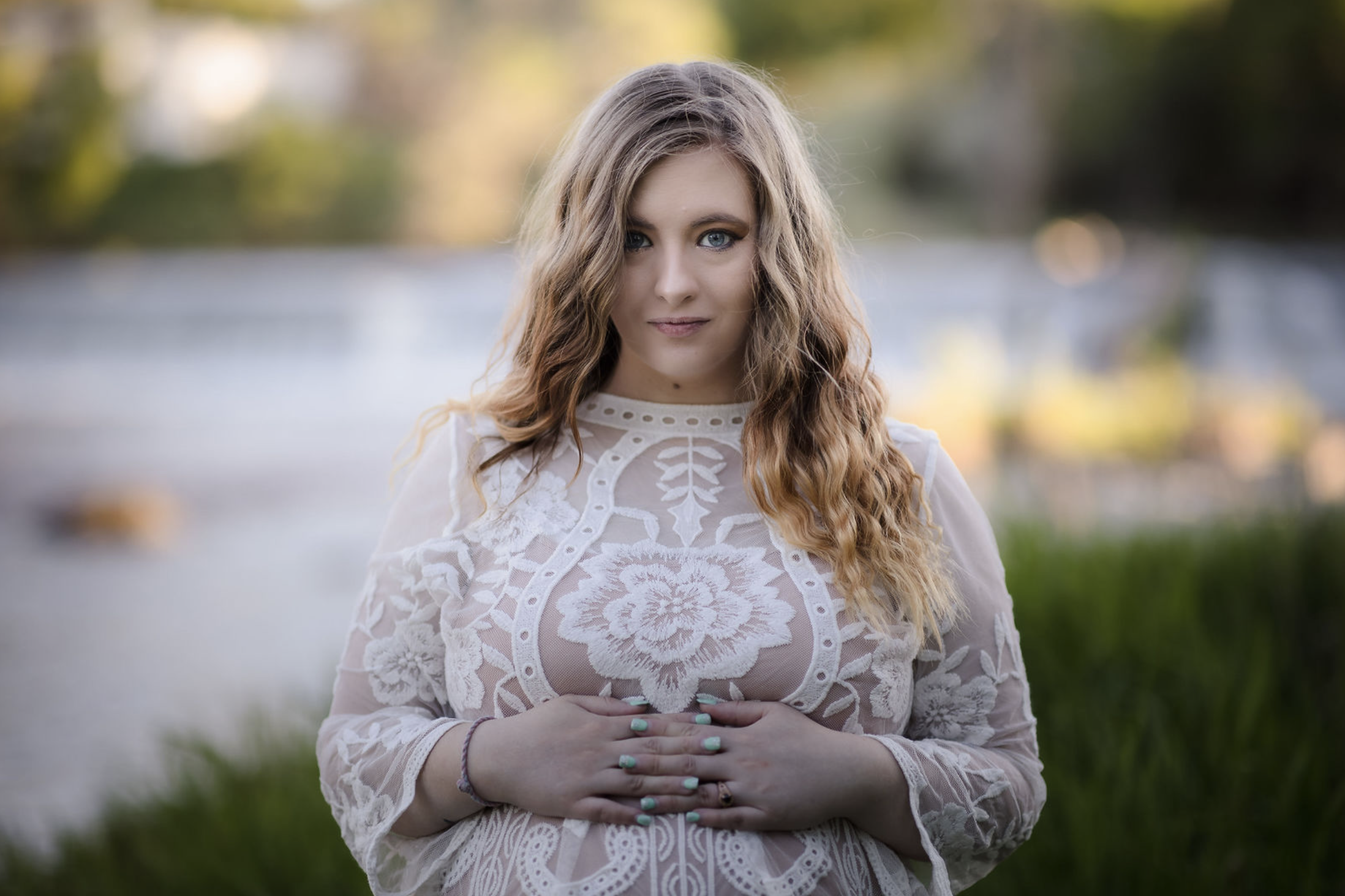 Two children playing near the edge of a lake during sunset, with trees in the background and the sun reflecting on the water.