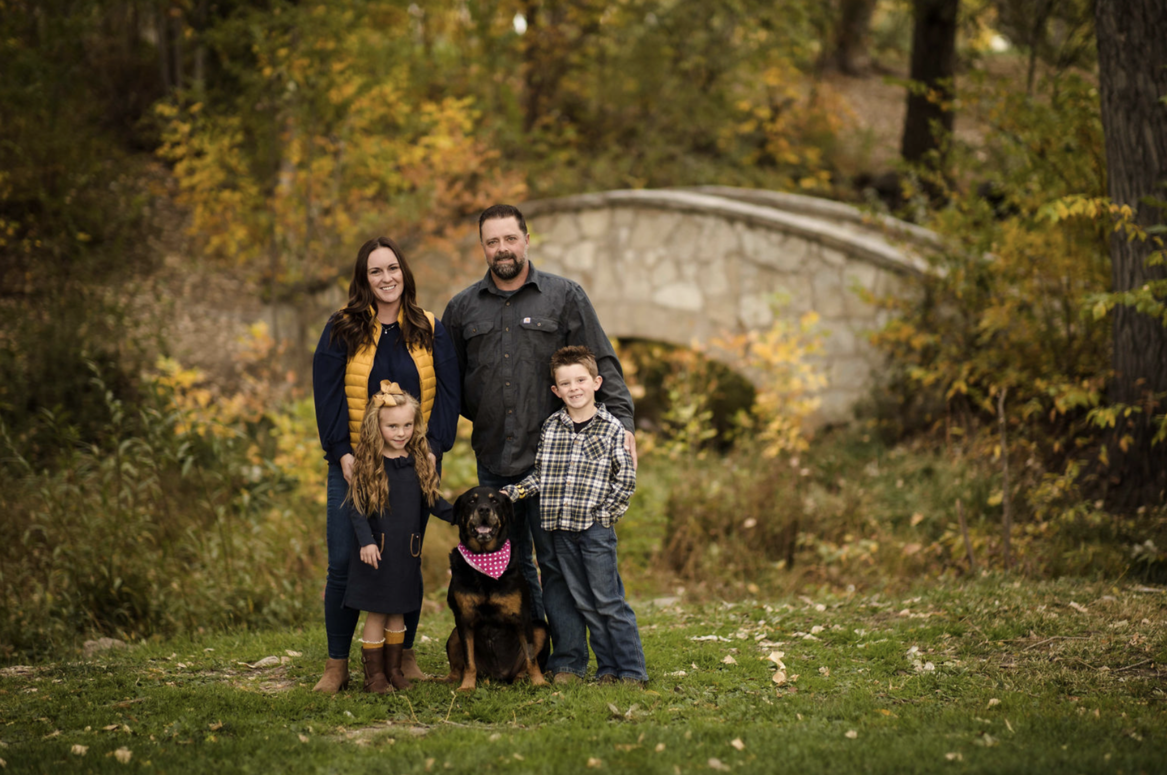Two children playing near the edge of a lake during sunset, with trees in the background and the sun reflecting on the water.
