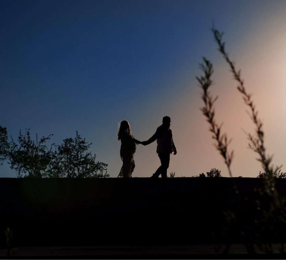 A pregnant woman in a yellow dress standing outdoors in a park at sunset, smiling and holding her belly, with trees and grass in the background.