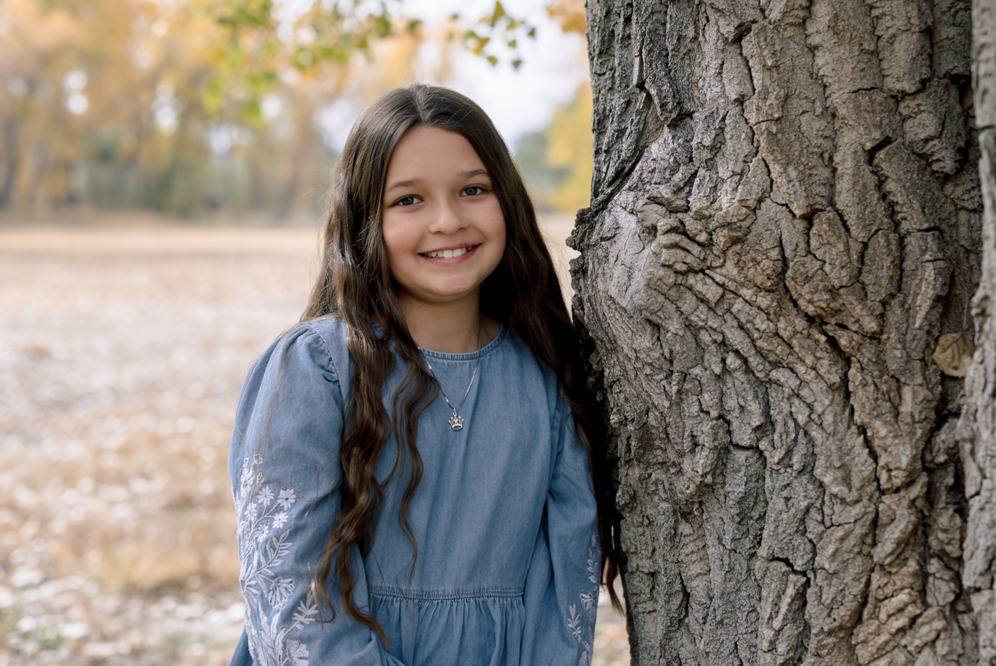 Two children playing near the edge of a lake during sunset, with trees in the background and the sun reflecting on the water.
