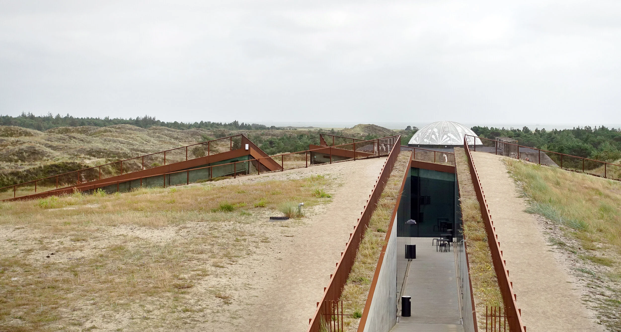 1 av totalt 4 innganger til museet. Sanddyner og furuskog i bakgrunnen.