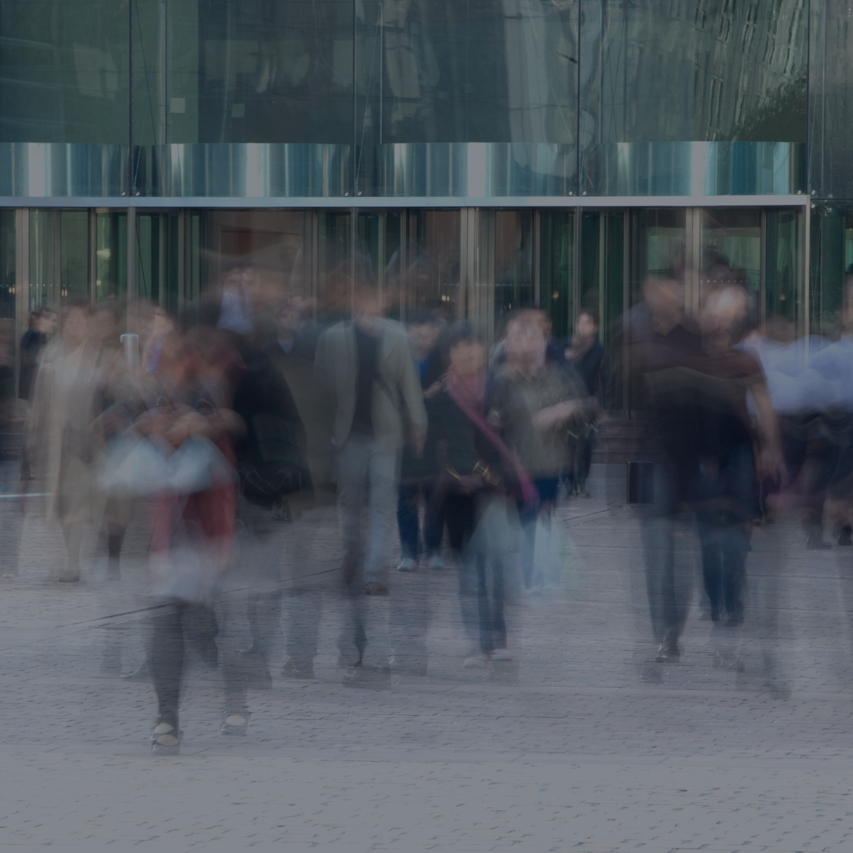 Blurred motion of a crowd of people walking outside a modern building with glass facade.