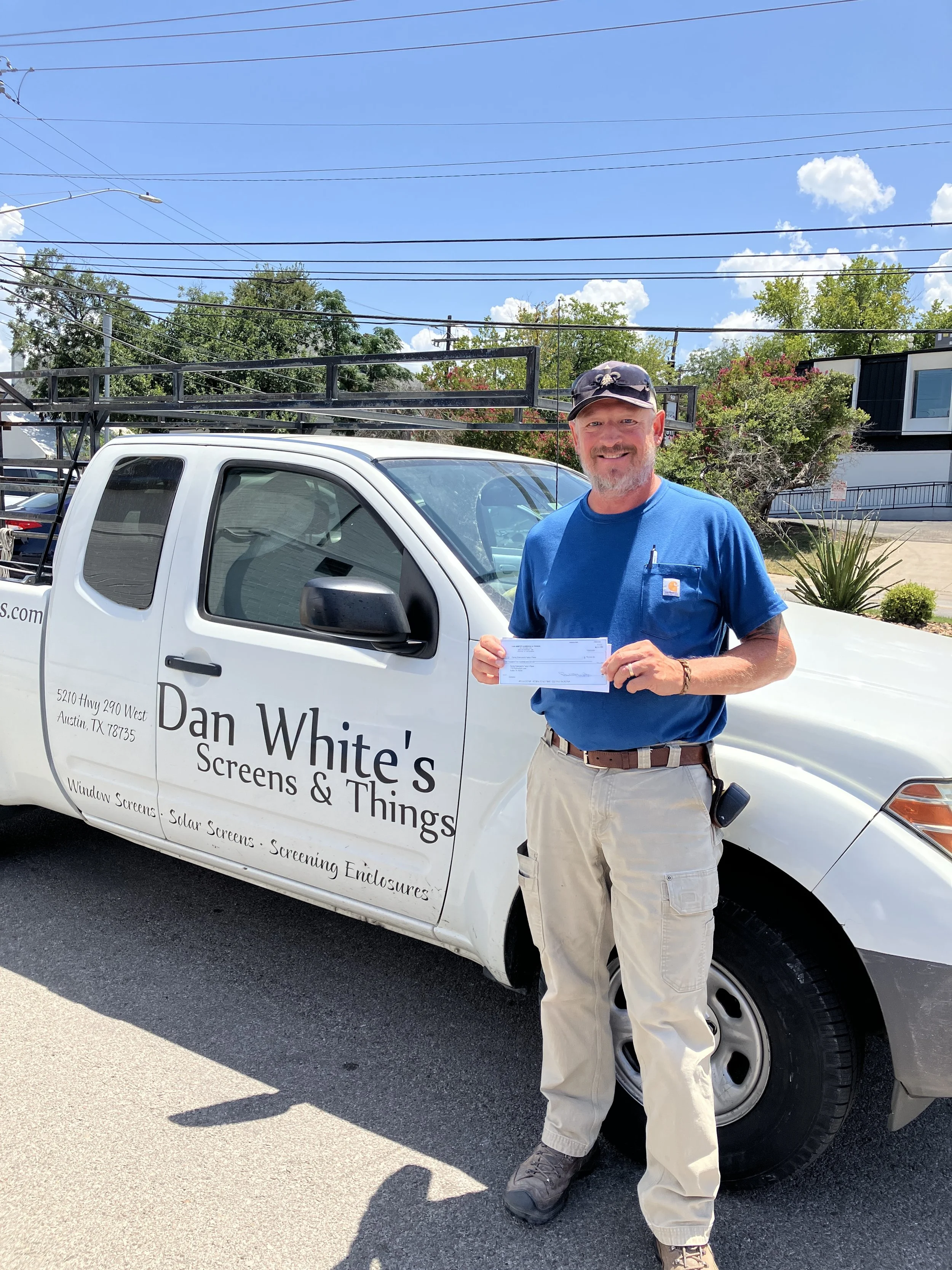 A person holding a check donation in front of the Dan White's Screens and Things truck