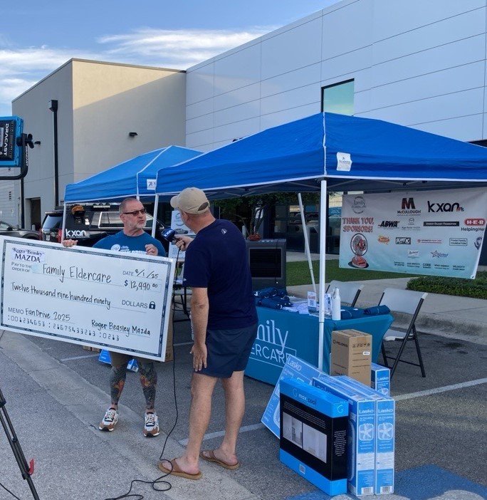A person holding a big check donation while another person is interviewing them.