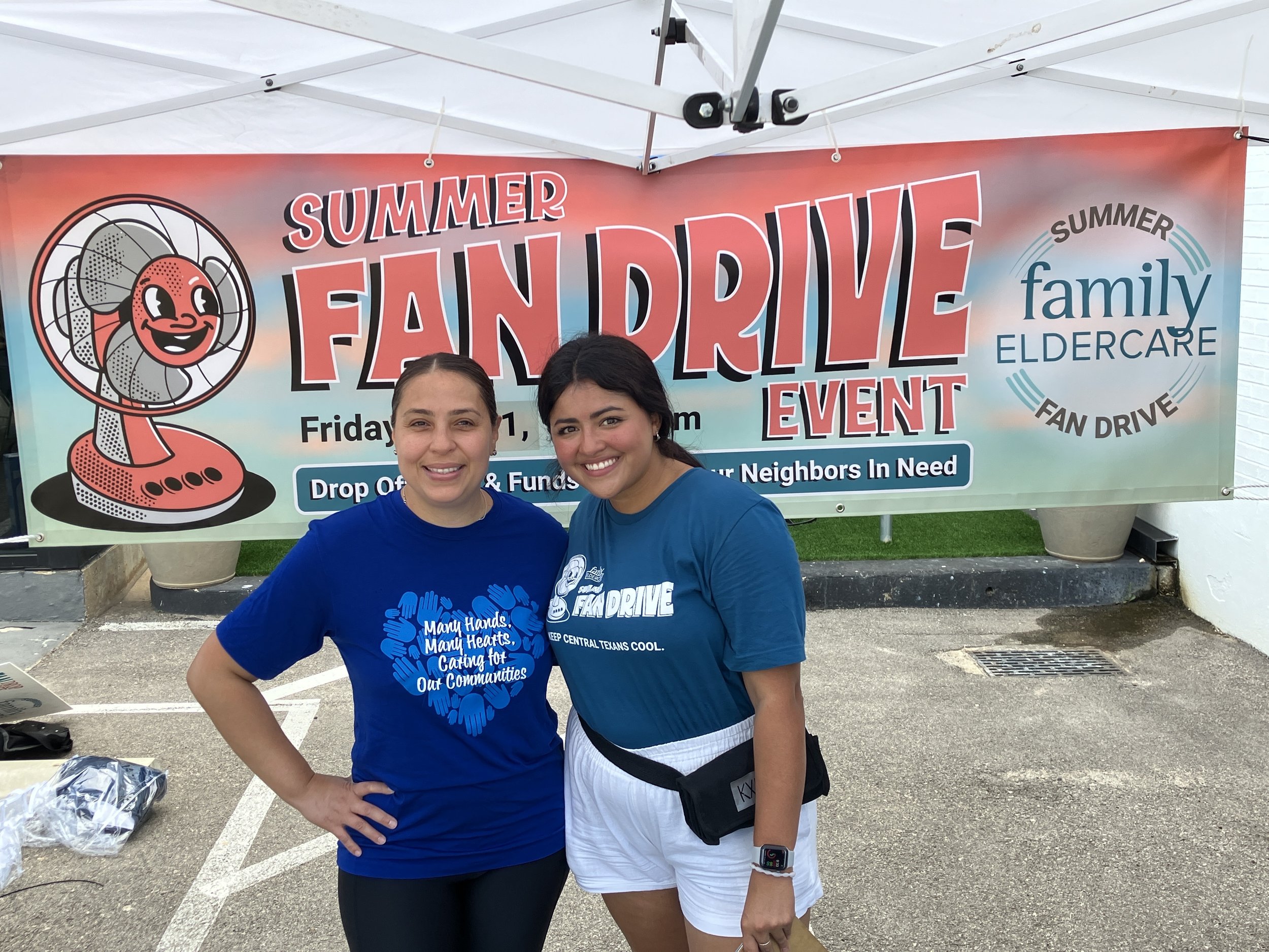 2 people standing under a tent in front of a Summer Fan Drive banner