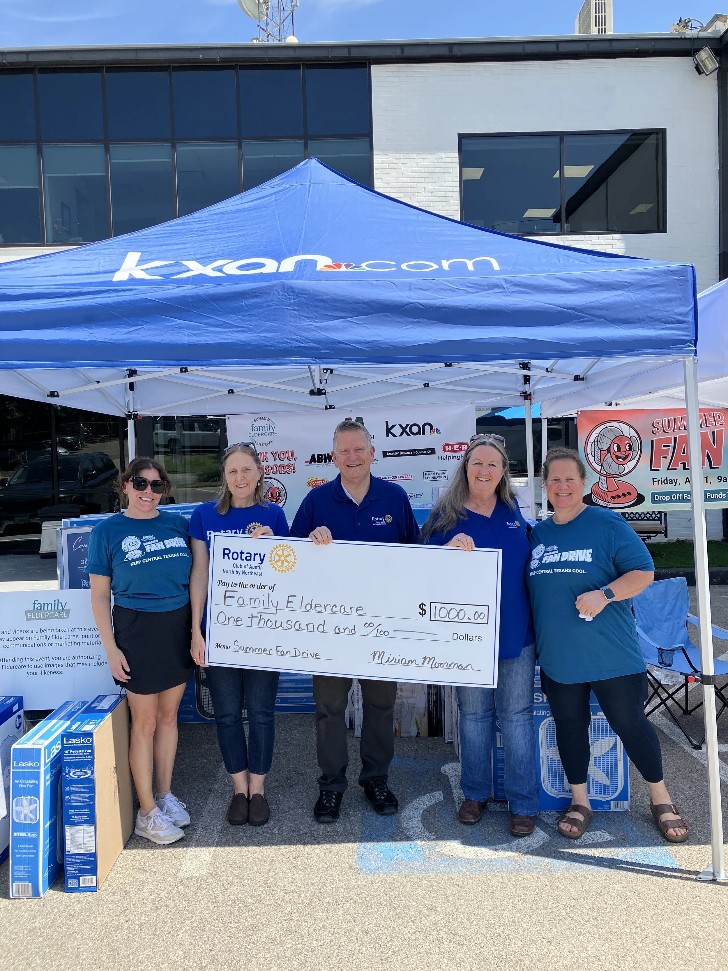 5 people holding a check donation under a tent