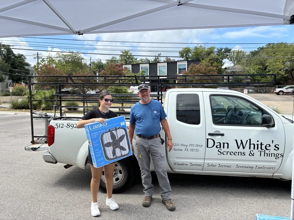2 people standing in front of a truck, one is holding a box fan