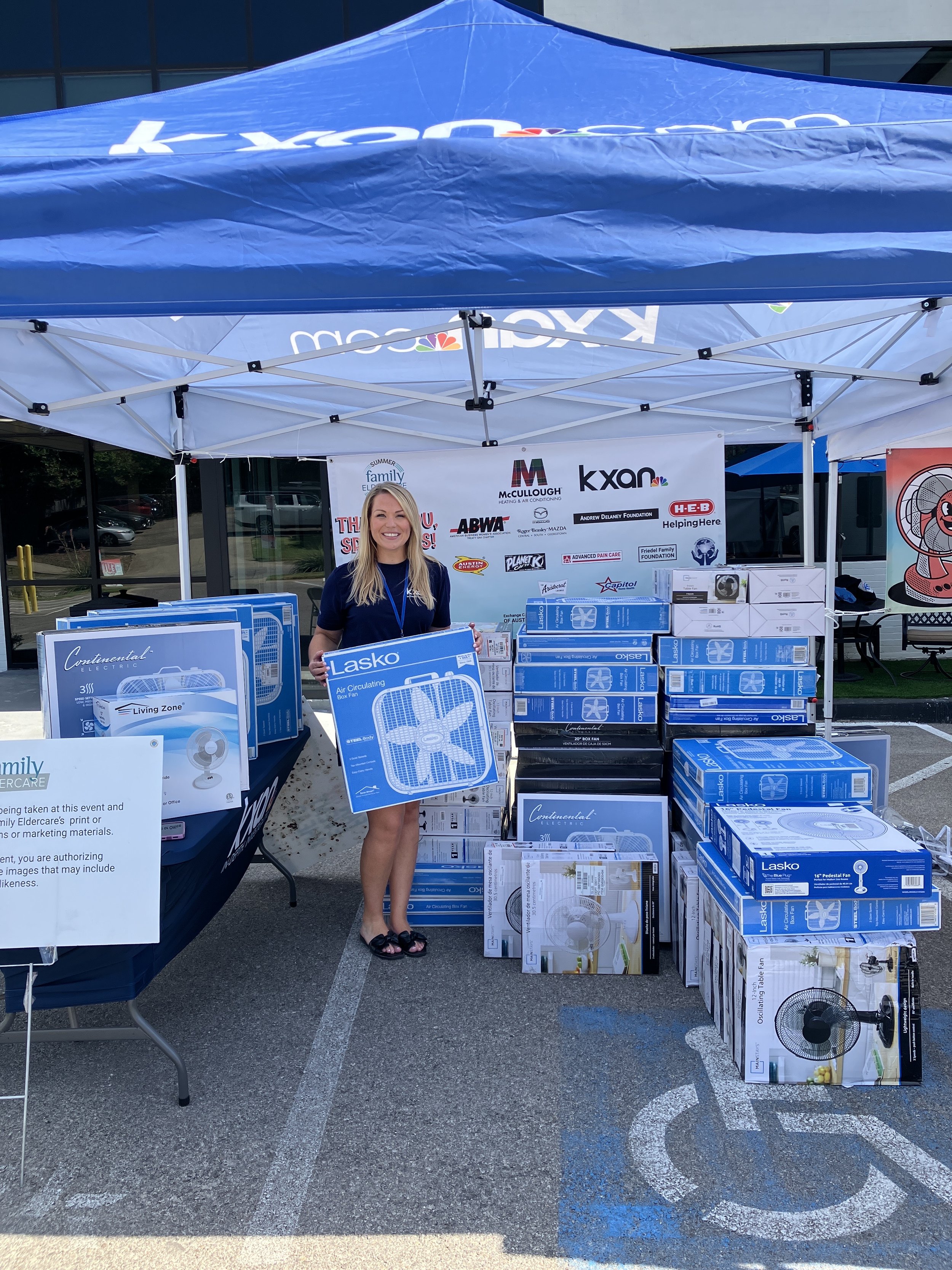 A person holding a fan and standing by a lot of fans under a tent