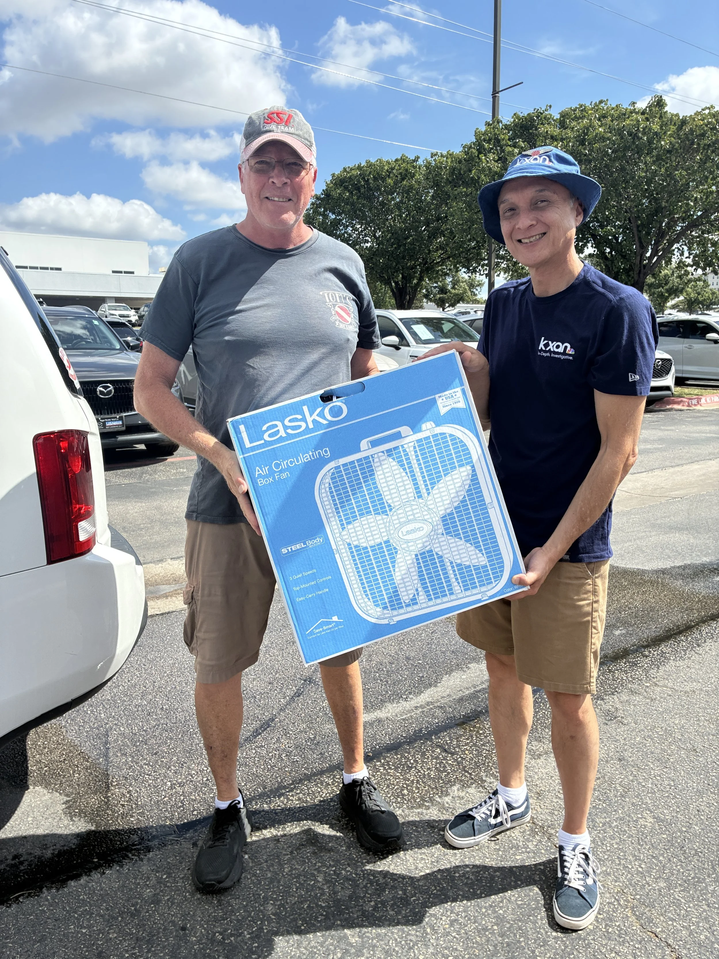 2 people standing holding a box fan