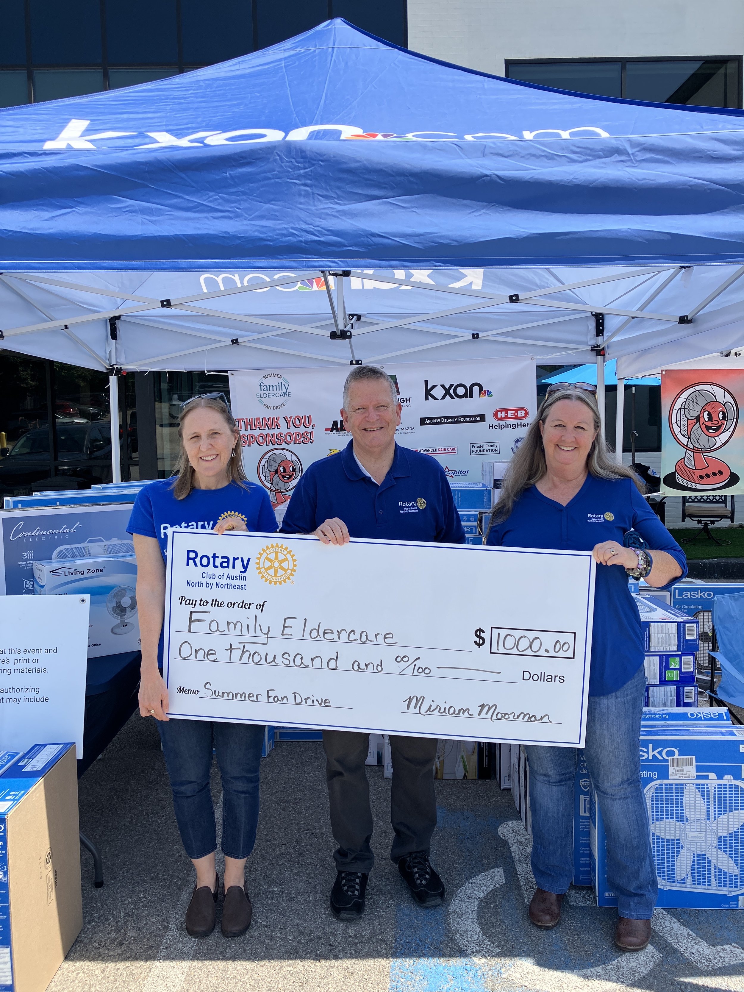3 people holding a check donation under a tent