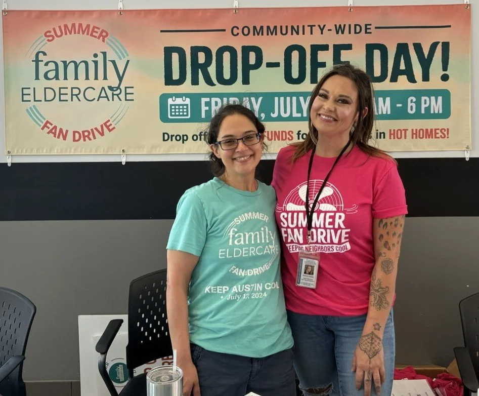 2 people standing in front of a sign that says Drop Off Day Family Eldercare Summer Fan Drive