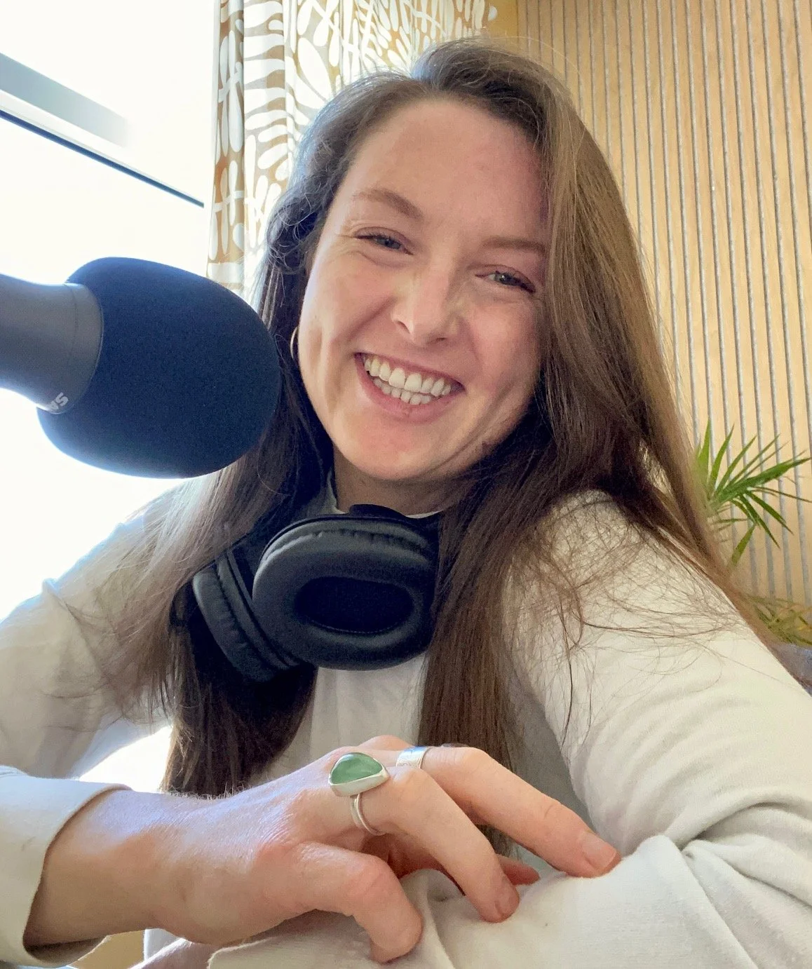 Sarah sitting in front of a microphone with headphones around her neck smiling