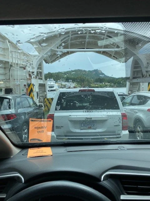 Looking out at other cars parked on a ferry deck with the ocean and an island in the distance
