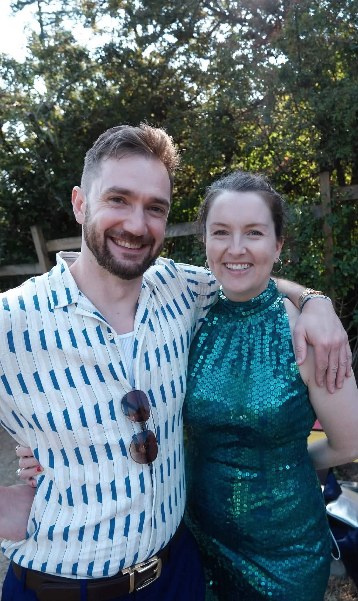 Sarah in a green sparkly dress smiling with her partner Nick outside in a garden