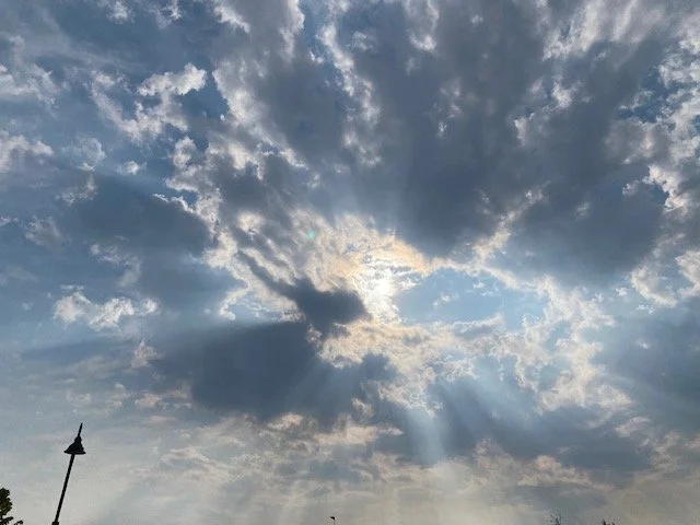 A light blue sky filled with clouds parting for bright rays of sunshine
