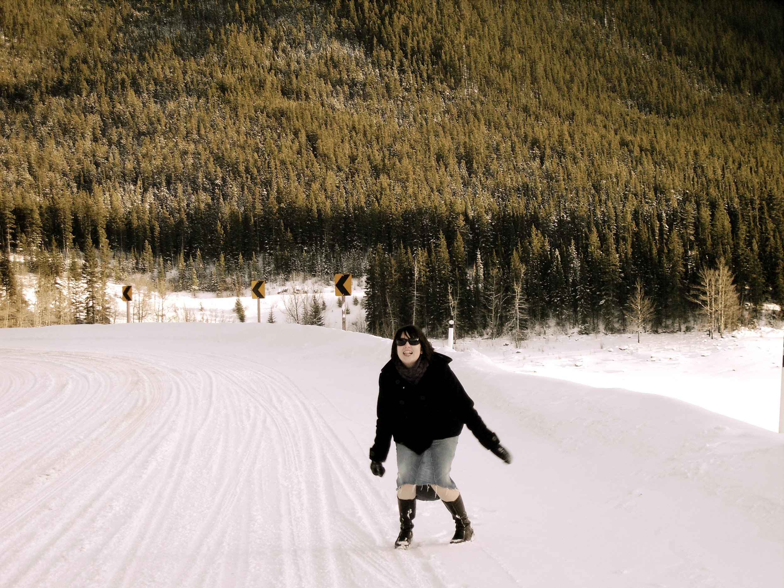 Sarah landing a jump in the middle of snow covered road with trees in the background