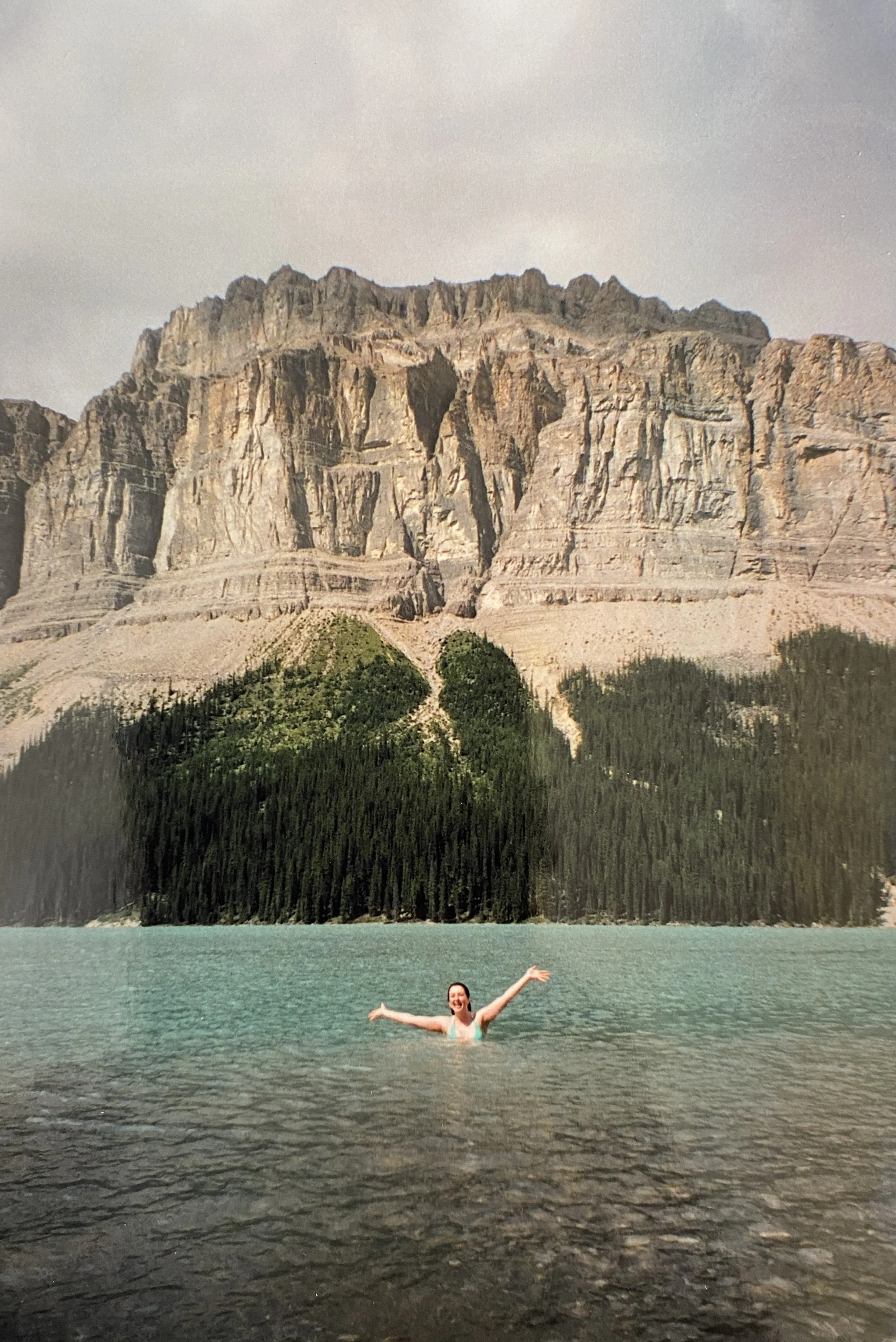 Sarah with her arms in the air in the middle of a crystal blue lake with mountains in the backgroun