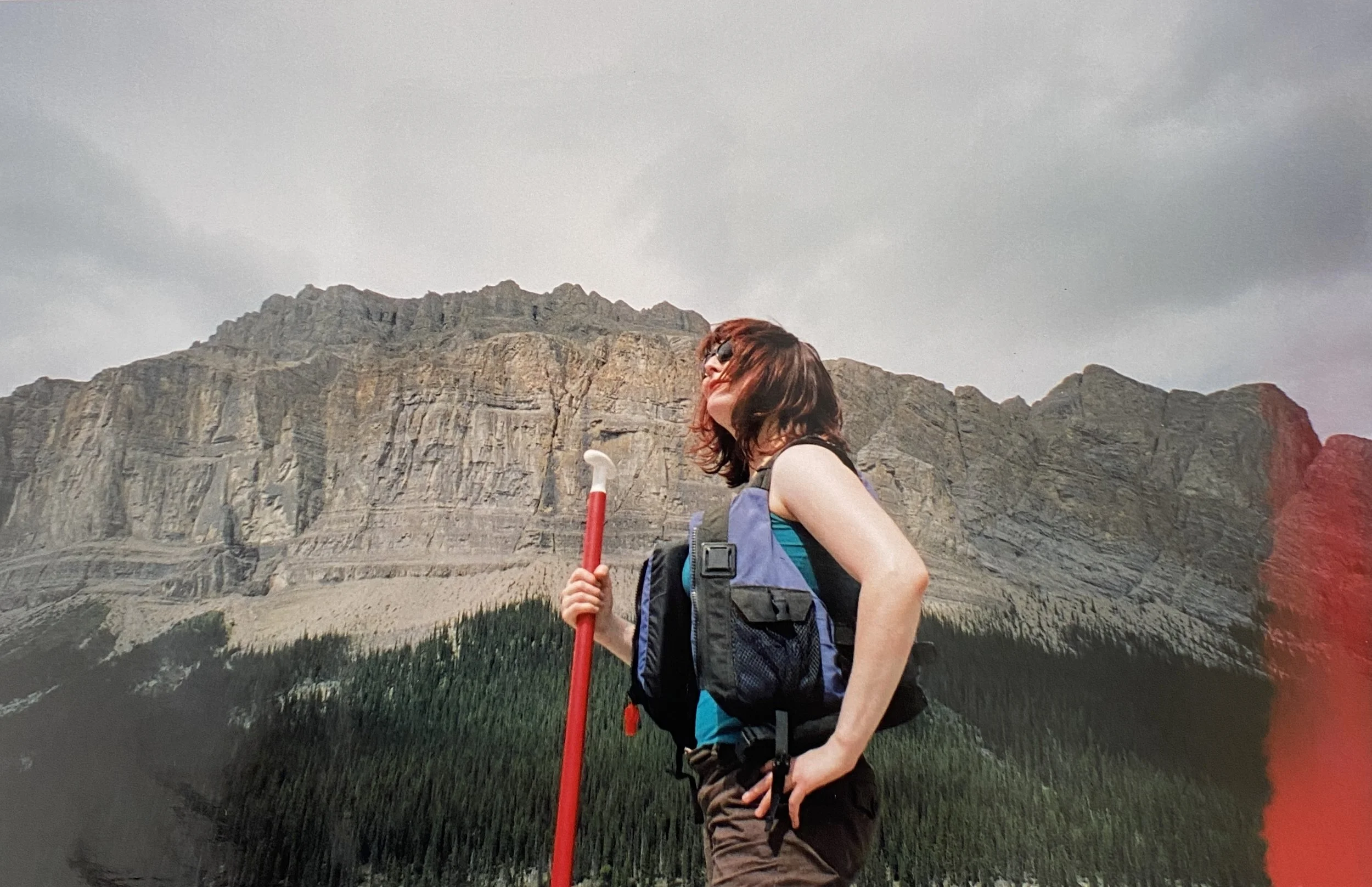 Sarah in a life vest holding a paddle looking to the sun with a mountain behind her