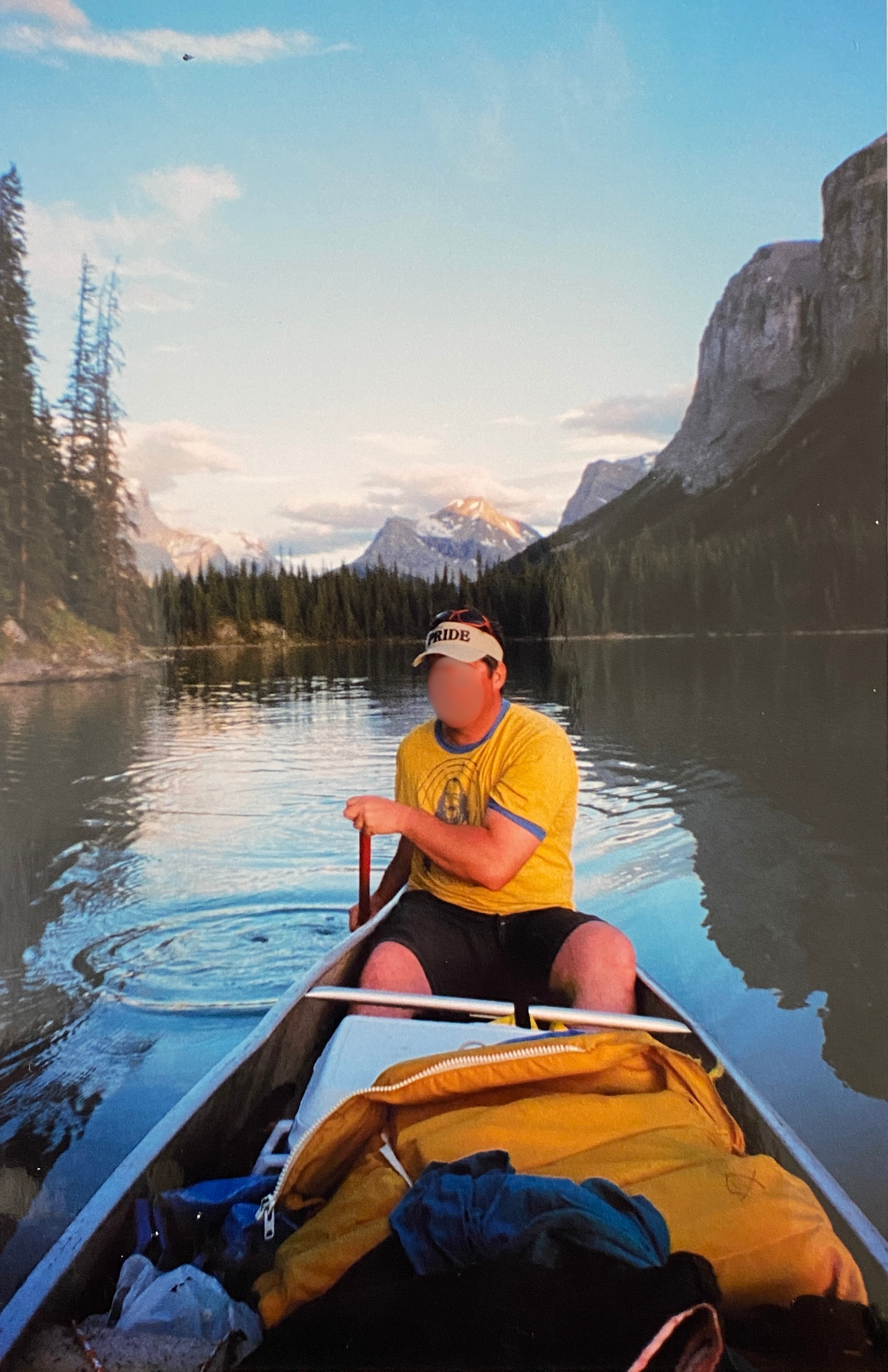 A man in a canoe holding a paddle one a still lake with an epic mountain range behind him