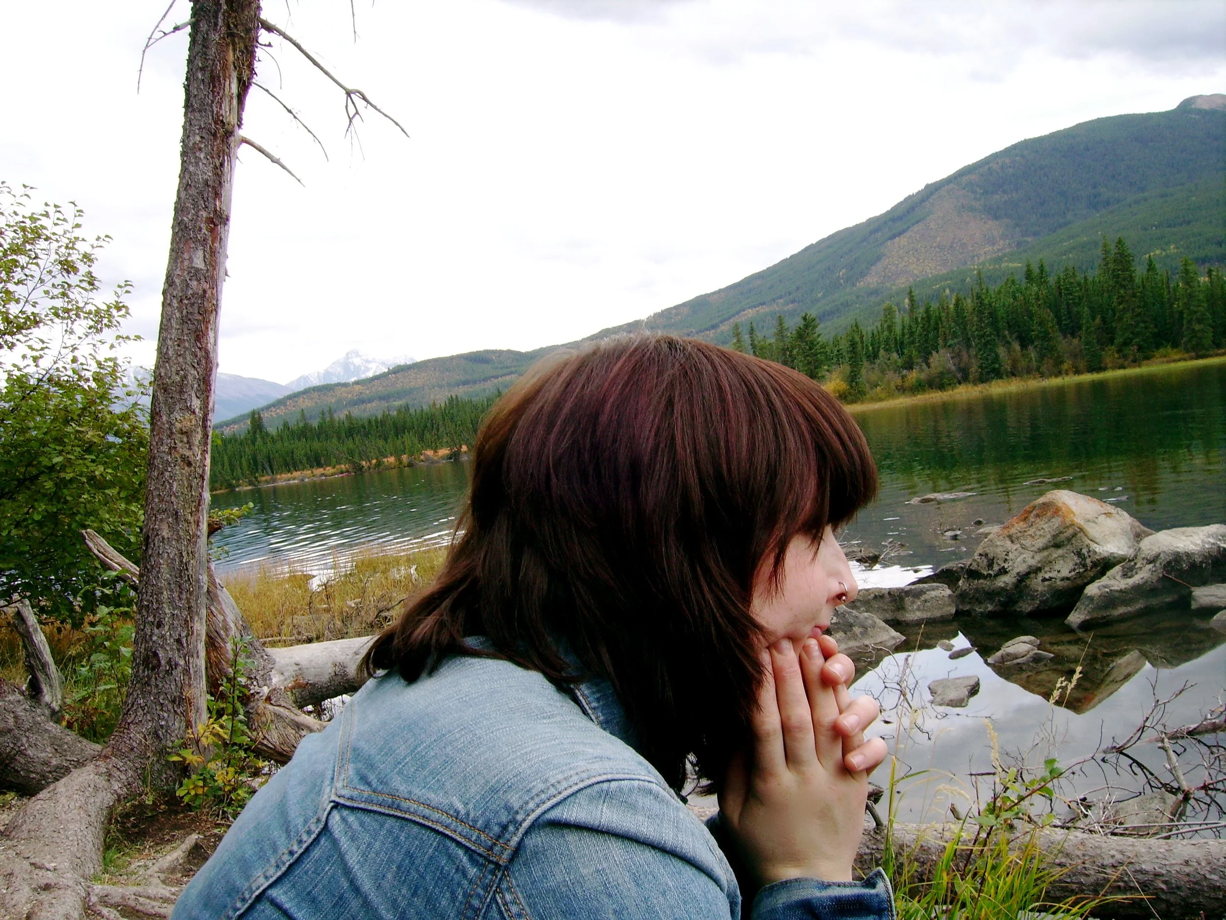 Sarah with red hair sitting on some rocks by a lake with a mountain in the background
