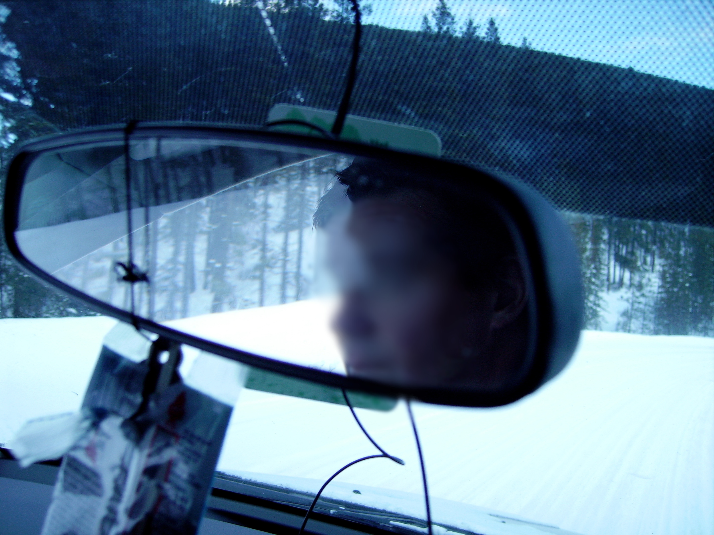 A man's blurry face in the reflection of a car's rearview mirror with snow and trees out the window