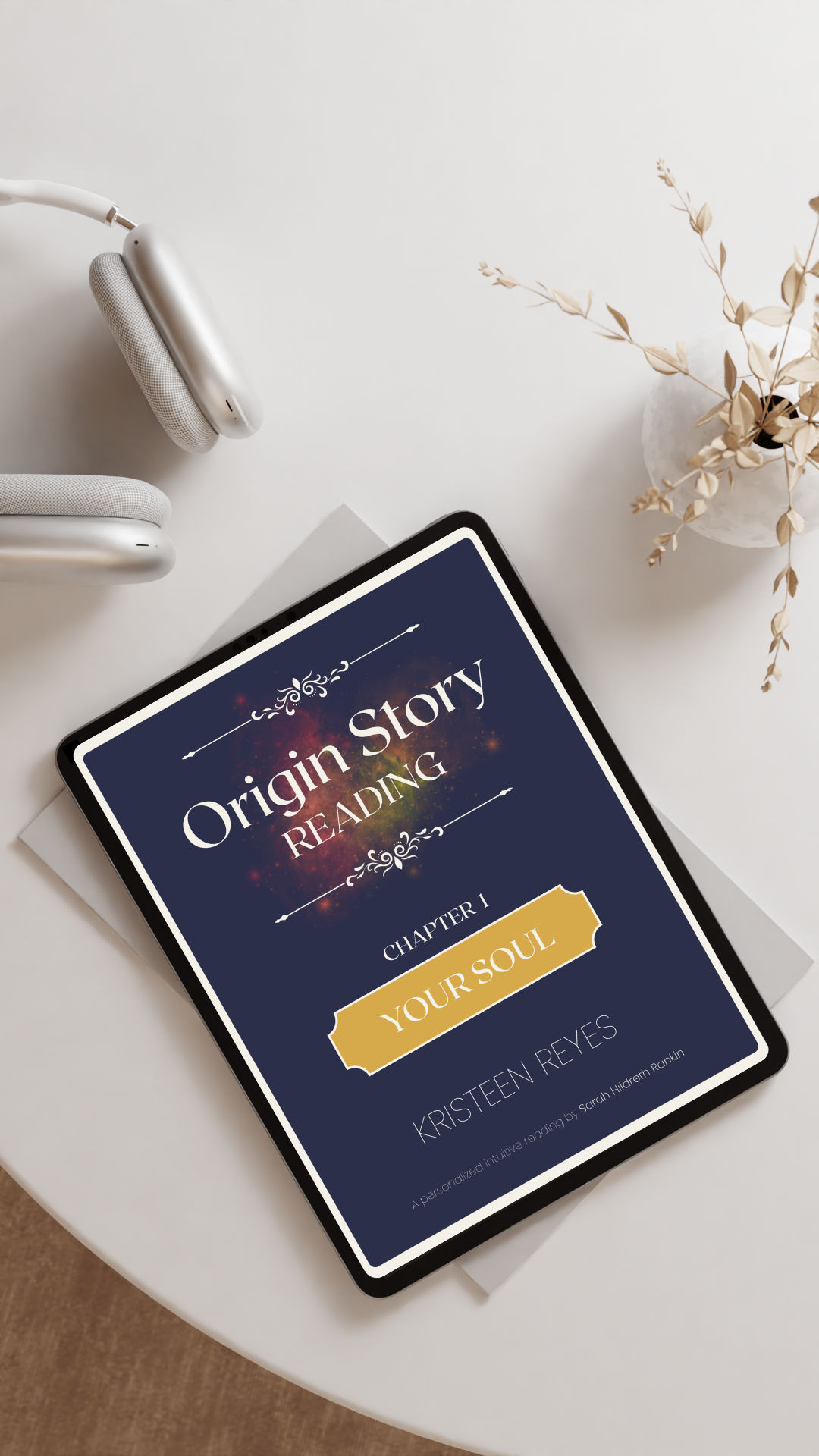 Digital tablet on a white table displaying an e-book titled 'Origin Story Reading: Chapter 1 Your Soul' by Kristteen Reyes, with a pair of white headphones and a white paper underneath, and a white vase with dried beige leaves to the right.