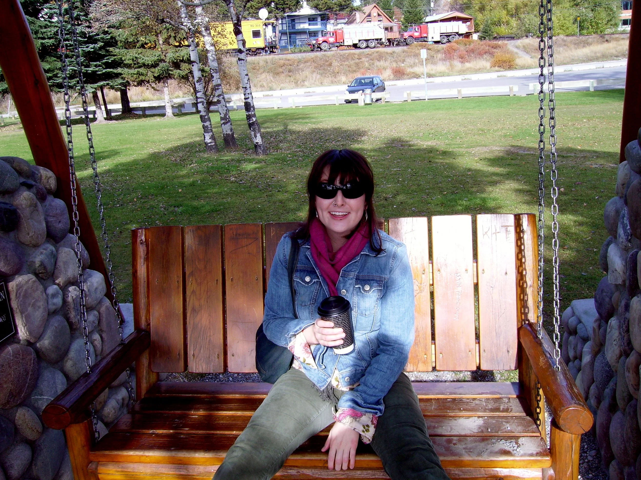 Sarah holding a coffee cup on an outdoor swing set in a rest stop by a highway