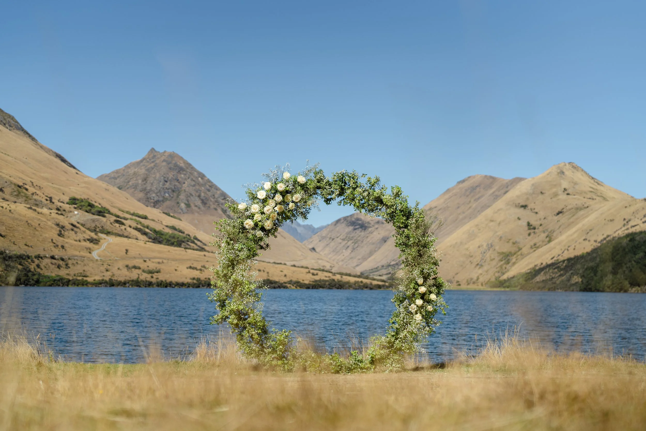 A circular arch decorated with lush foliage set up at Moke Lake for a small wedding