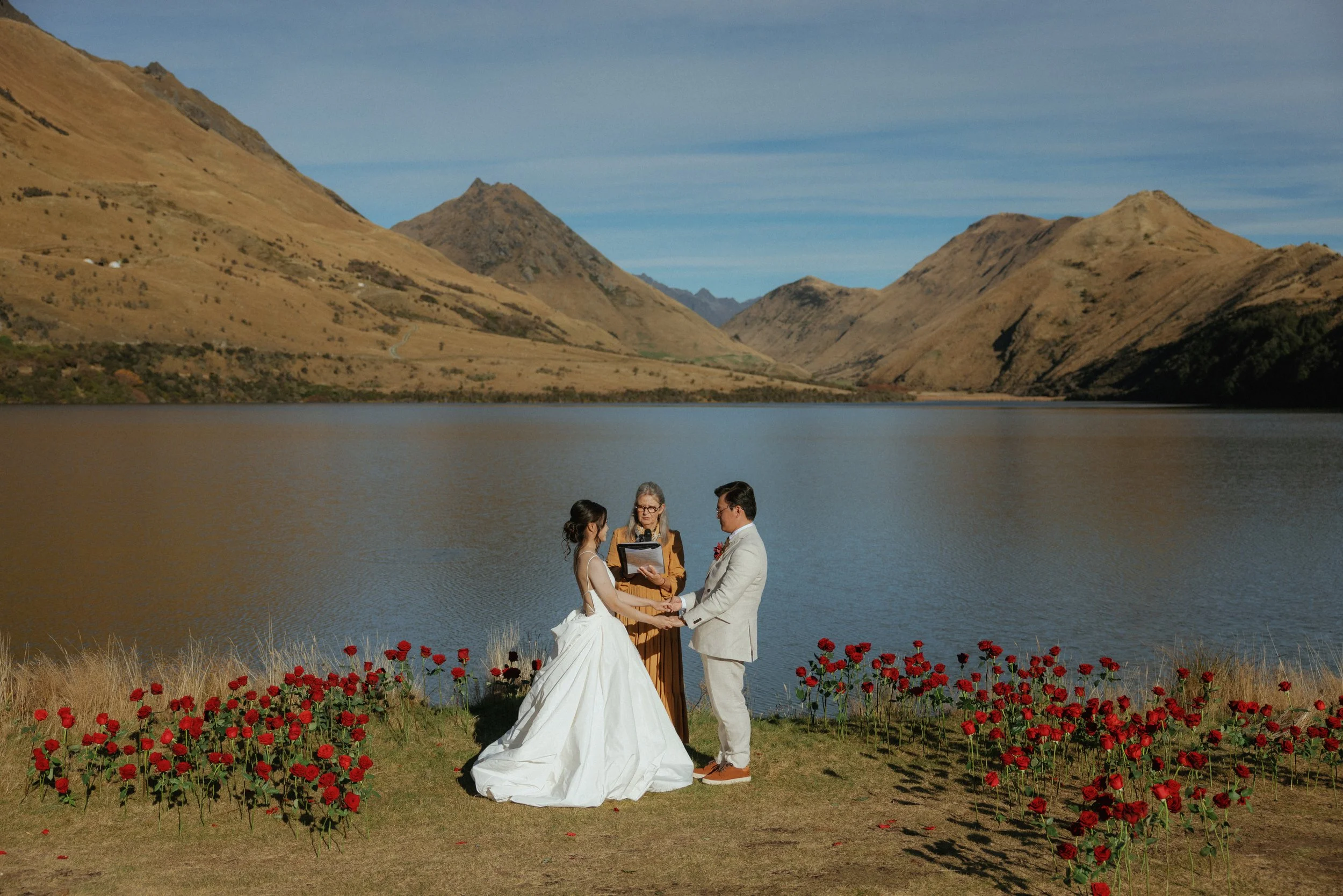 A couple is having a beautiful wedding ceremony at Moke Lake, Queenstown, New Zealand