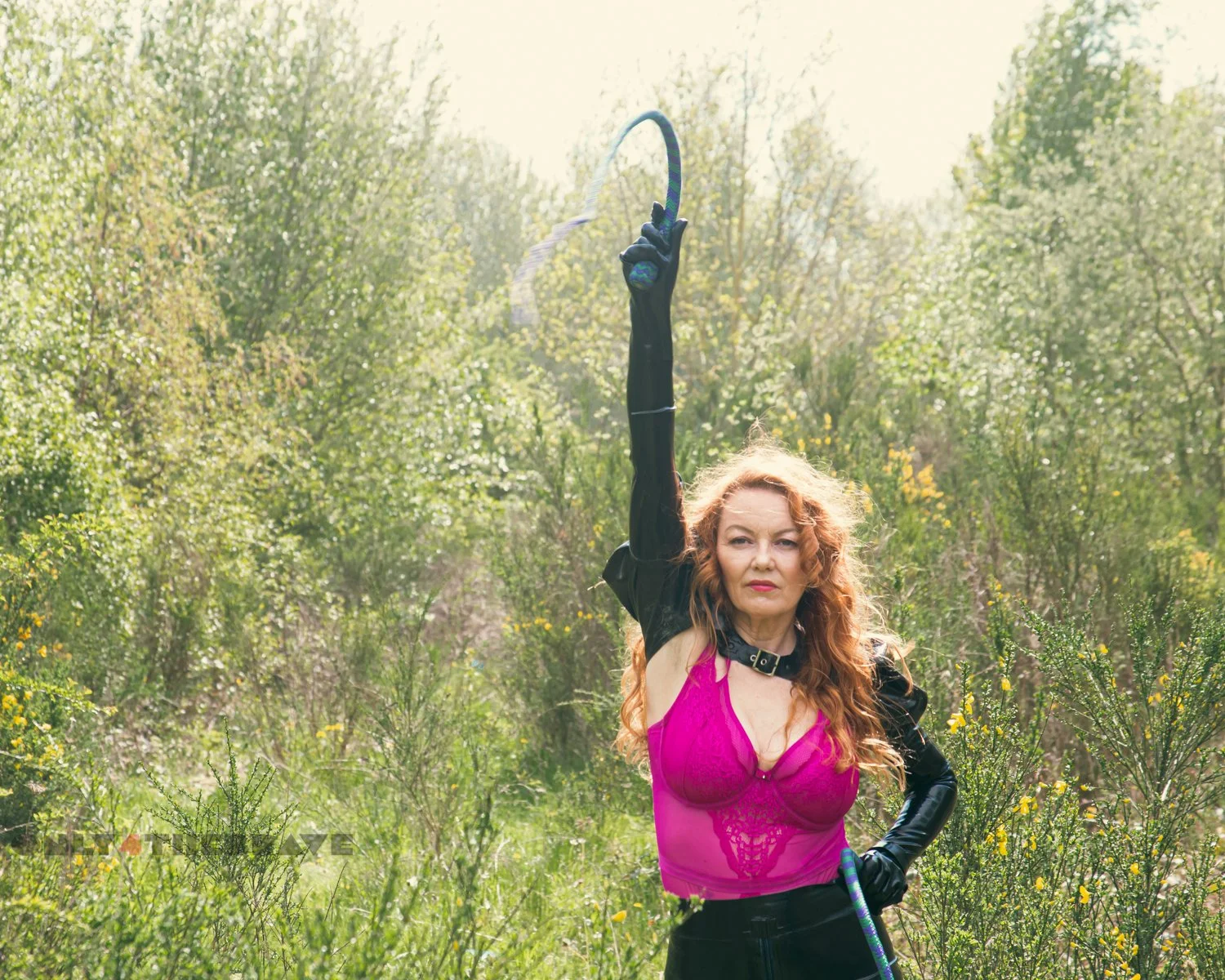 A photograph of a woman holding a bull whip wearing lingerie and a latex open front skirt