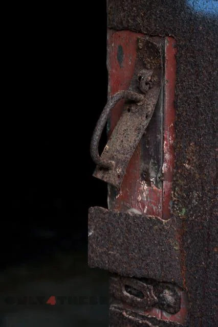Close-up of a rusty metal door latch on a weathered wooden surface.