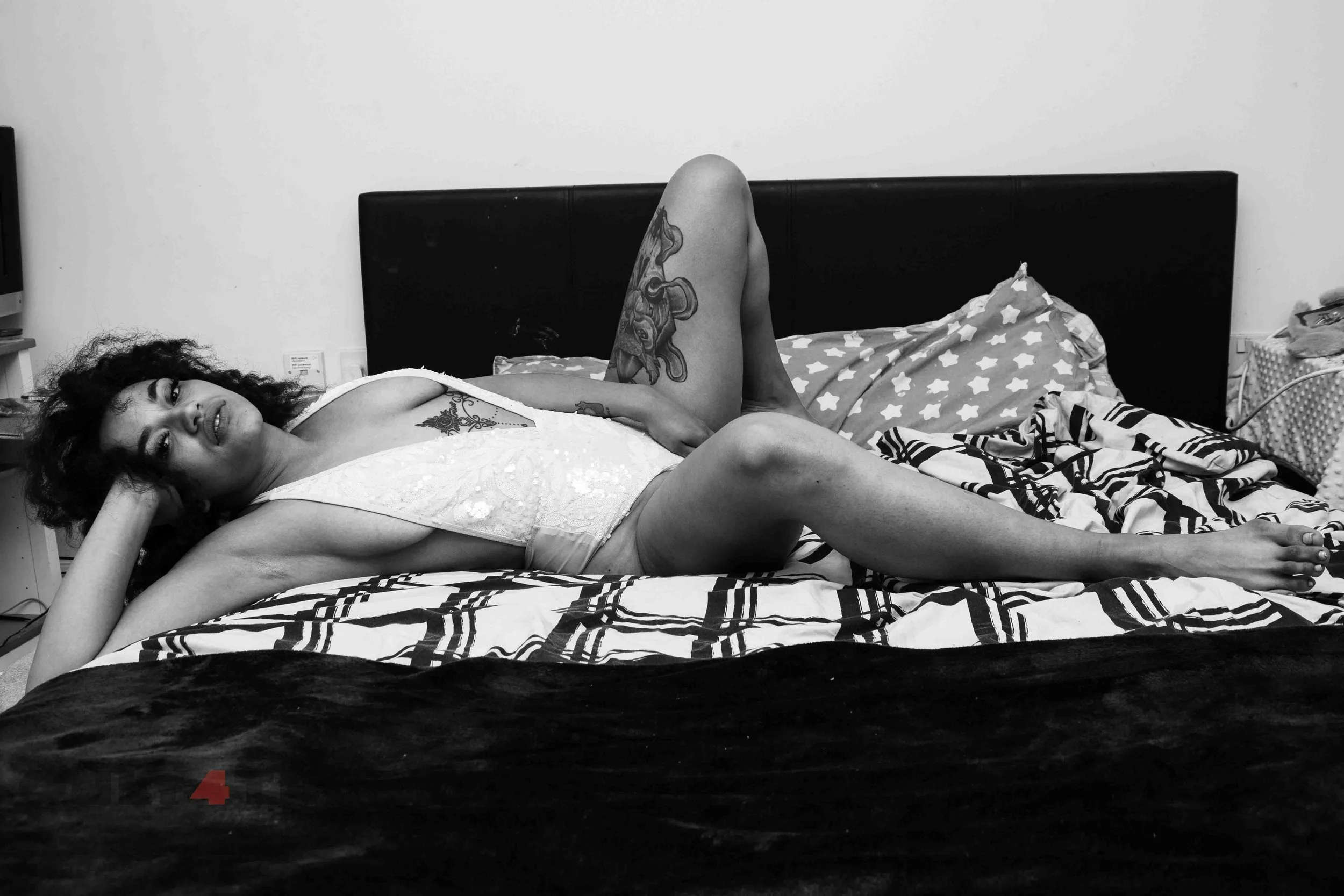 A clothed woman lying across the bed looking into the camera