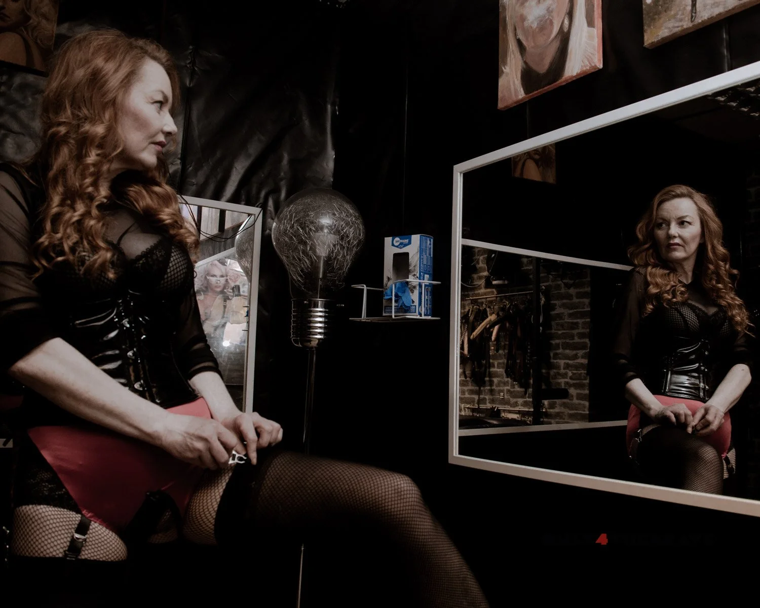 a photograph of a mistress fixing her suspenders as she looks at herself in the mirror