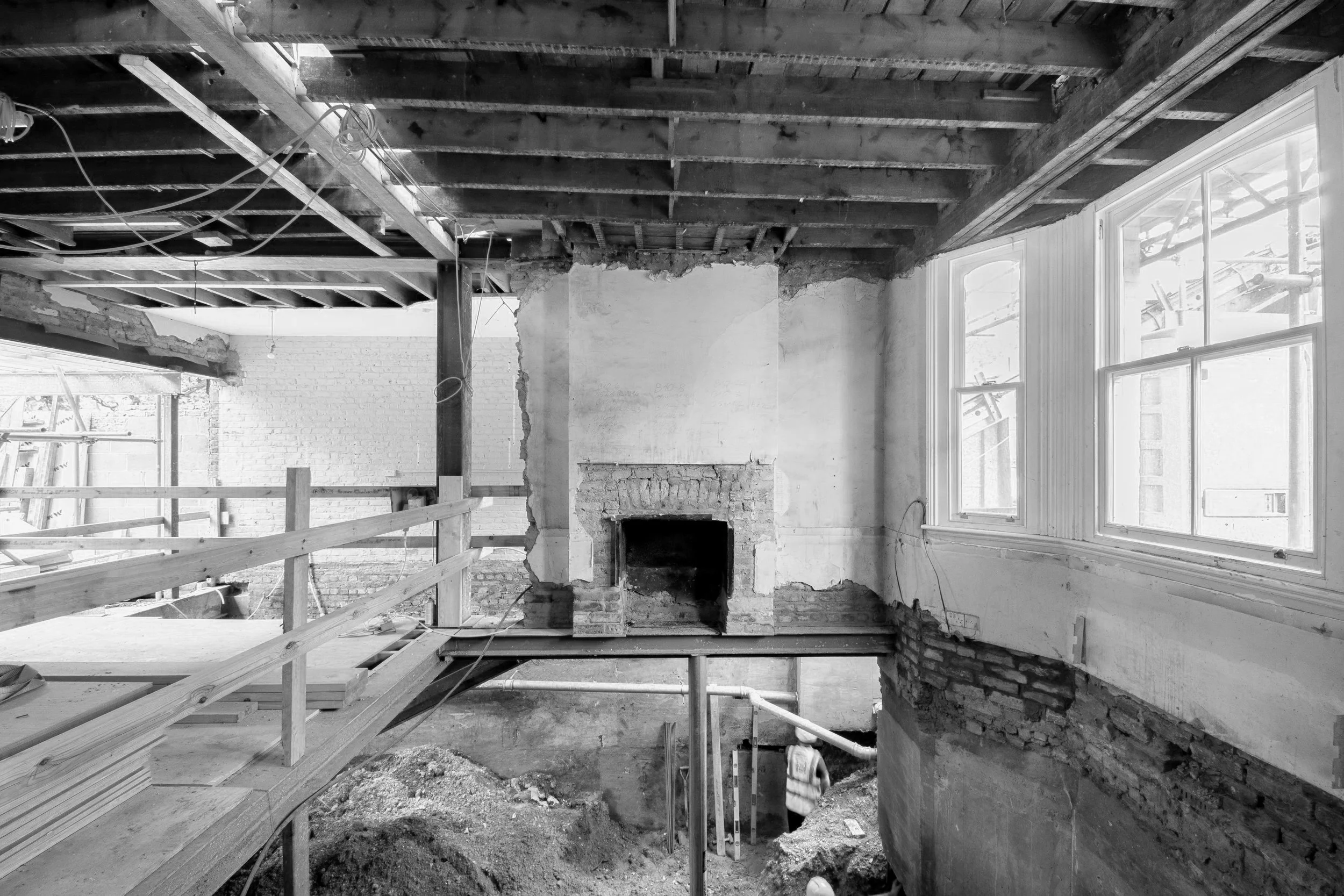Interior of a house under renovation, with exposed brick fireplace, construction workers, and scaffolding.