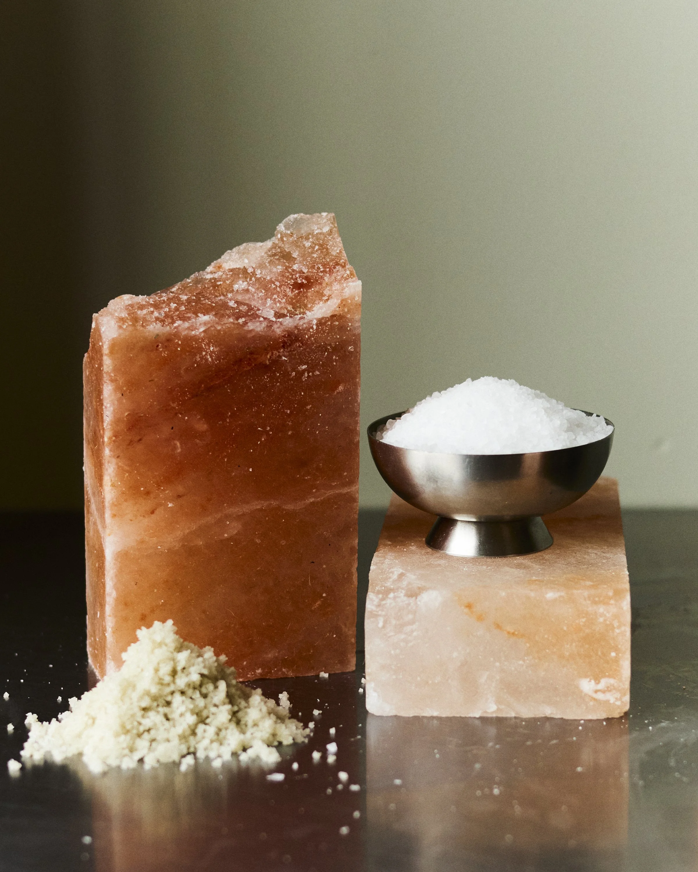 Salt and salt blocks on a reflective surface, with a bowl of salt on a salt block in the background.