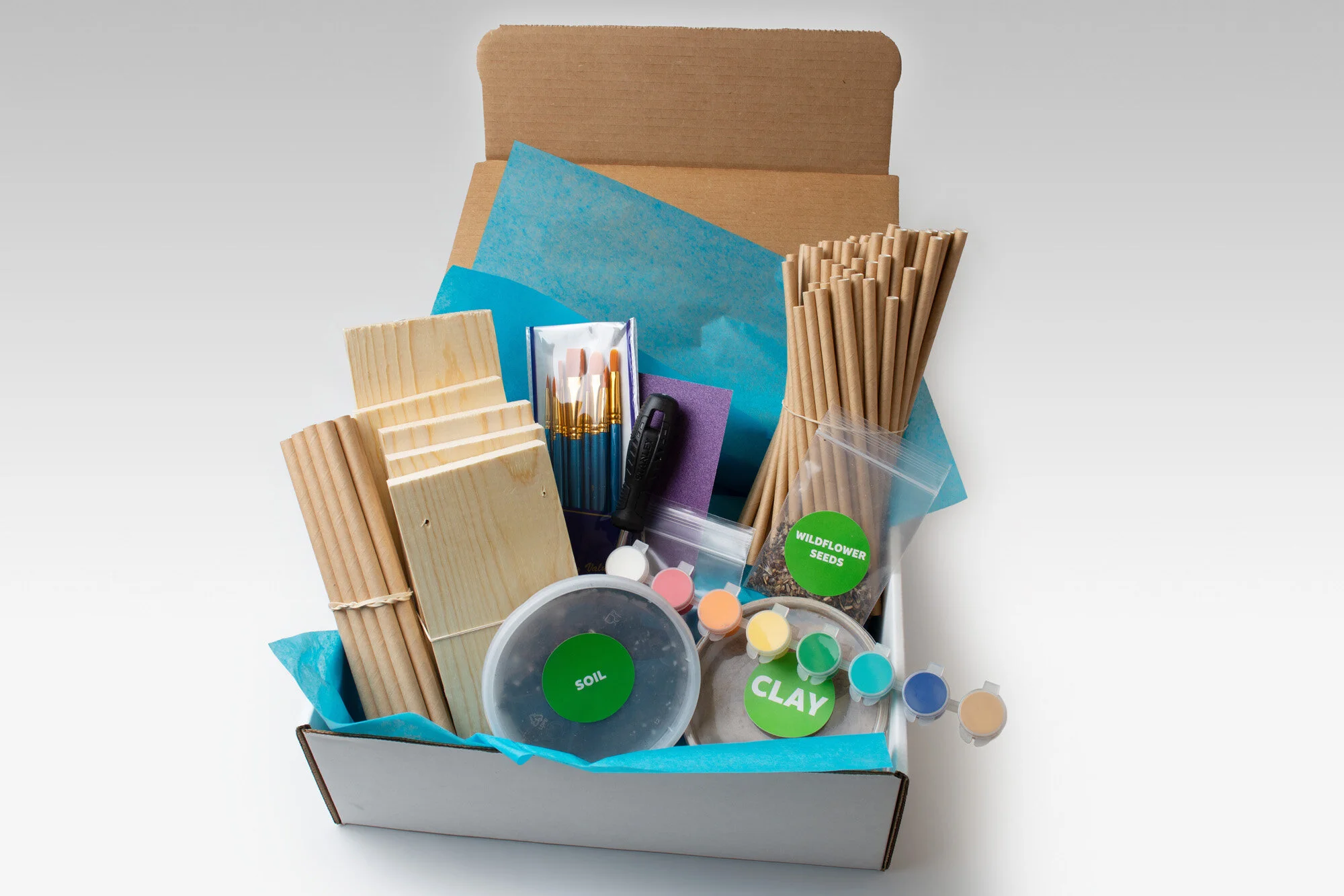 STEM kit with components for experiments, including wires, batteries, propellers, colored clay, instructional booklets, and paper envelopes, in an open box.
