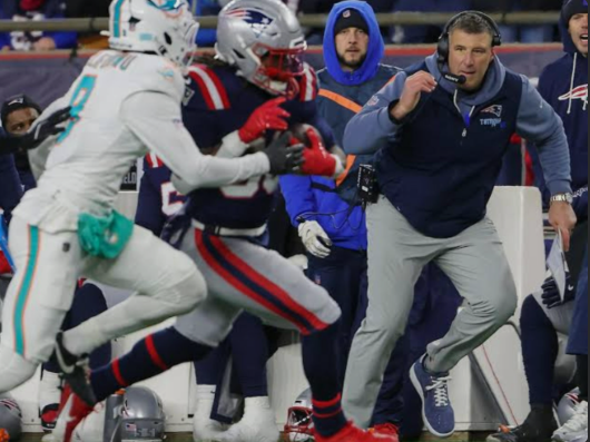 New England Patriots head coach and player in motion on the sideline during live play, illustrating leadership, preparation, and execution under pressure.