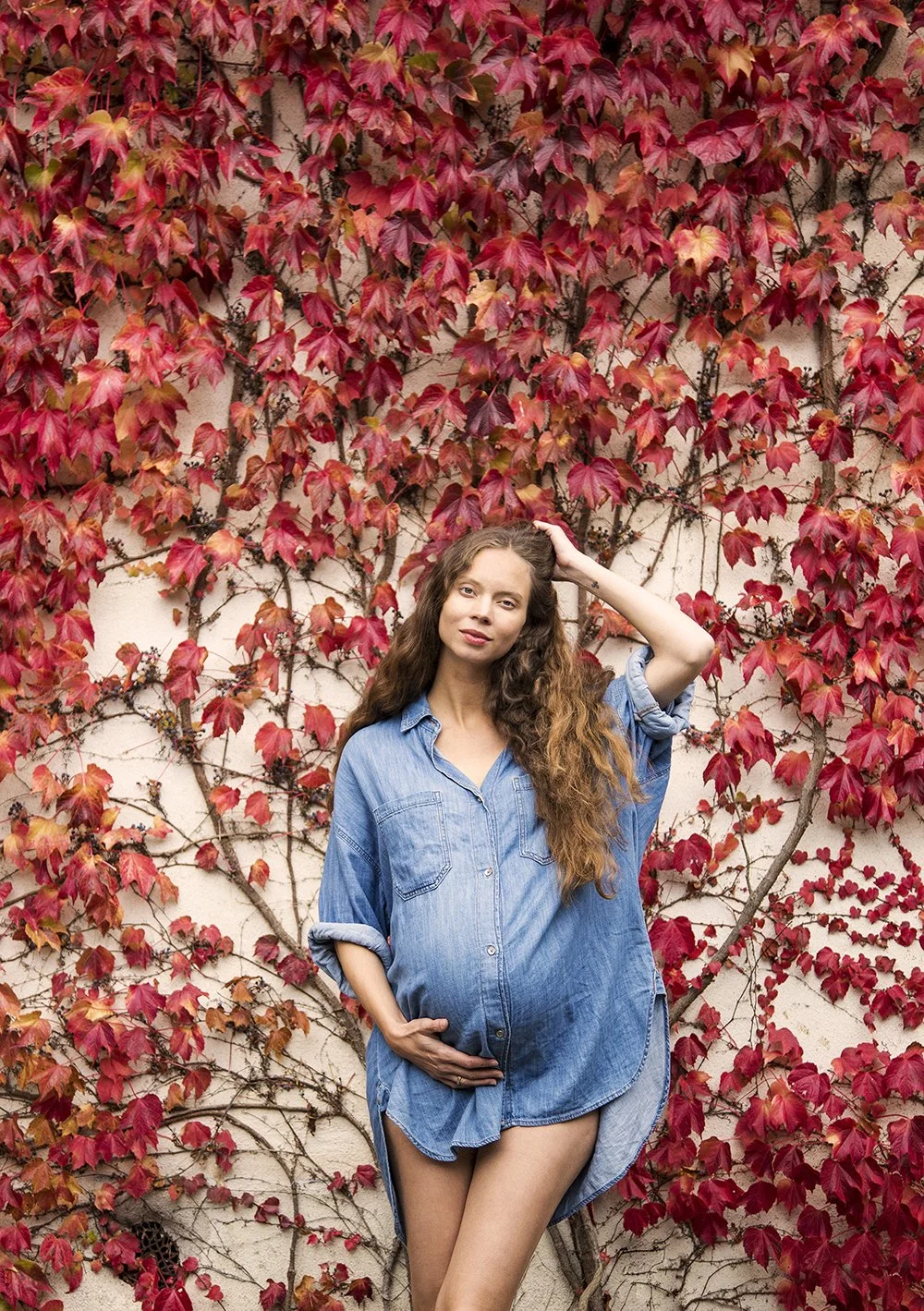 Pregnant woman in denim shirt on red leaf background