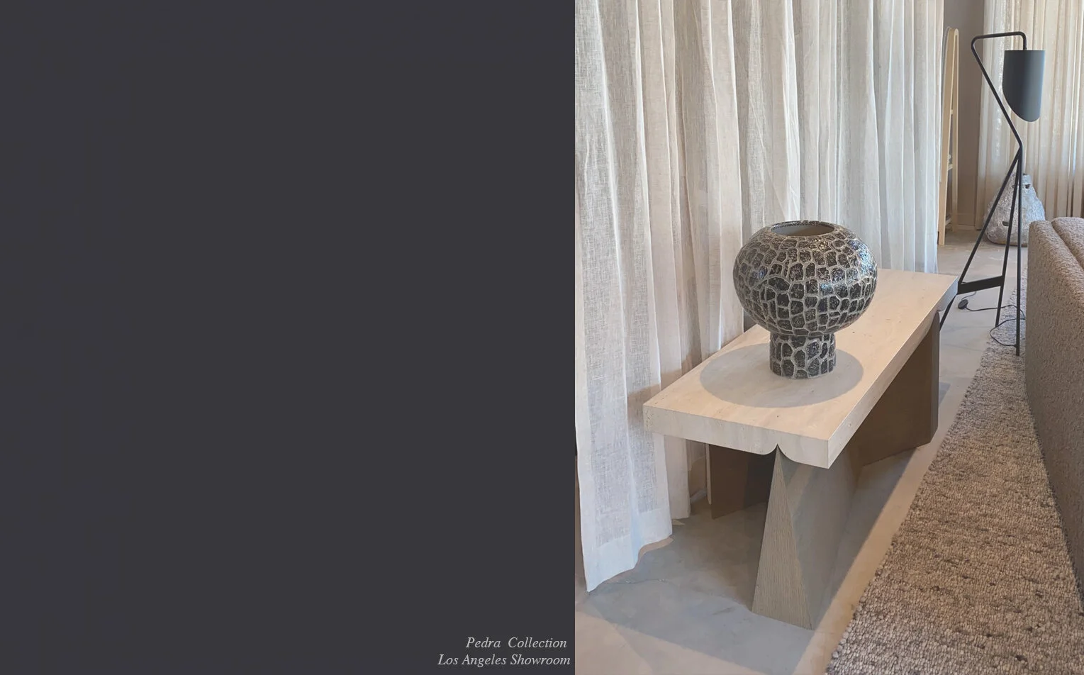 A decorative stone vase on a beige console table near a window with white curtains, with a black floor lamp next to a beige sofa in a modern living room.