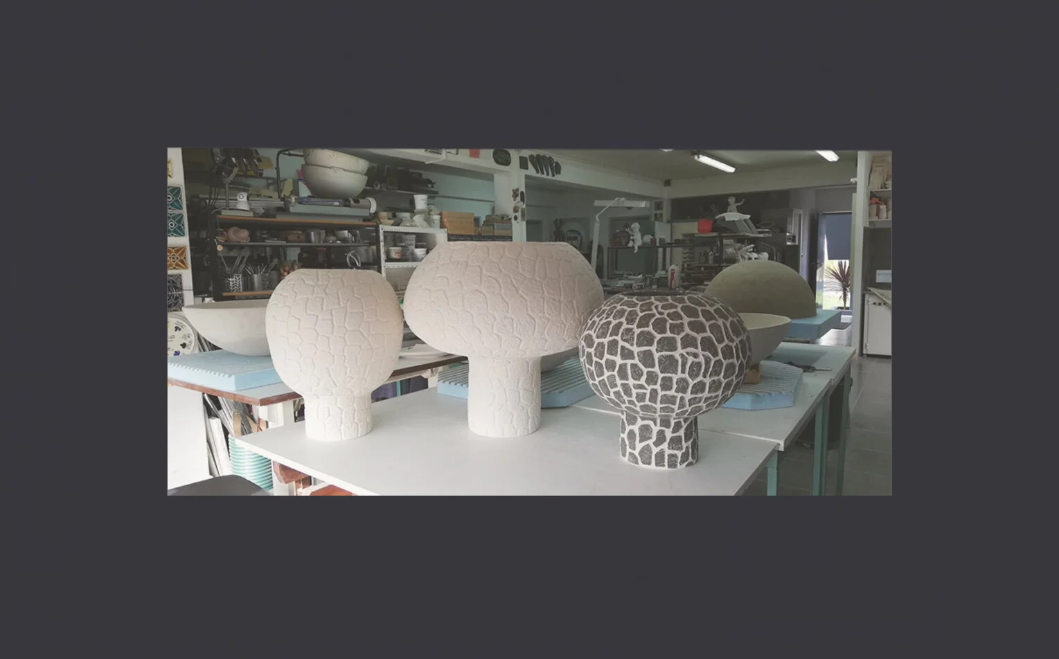 Ceramic sculptural vases with textured patterns in white and black, placed on a worktable inside a pottery studio.