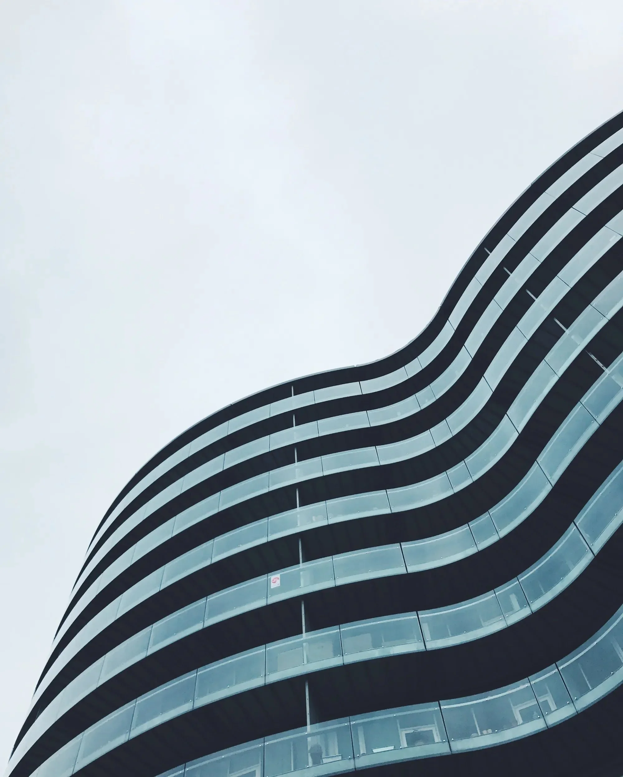 A modern multi-story building with a wavy architectural design, featuring curved glass balconies and a sleek exterior.