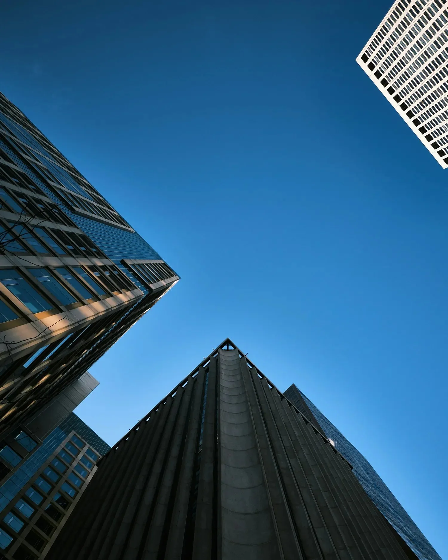 Looking up at tall modern office buildings with glass and concrete facades against a clear blue sky.