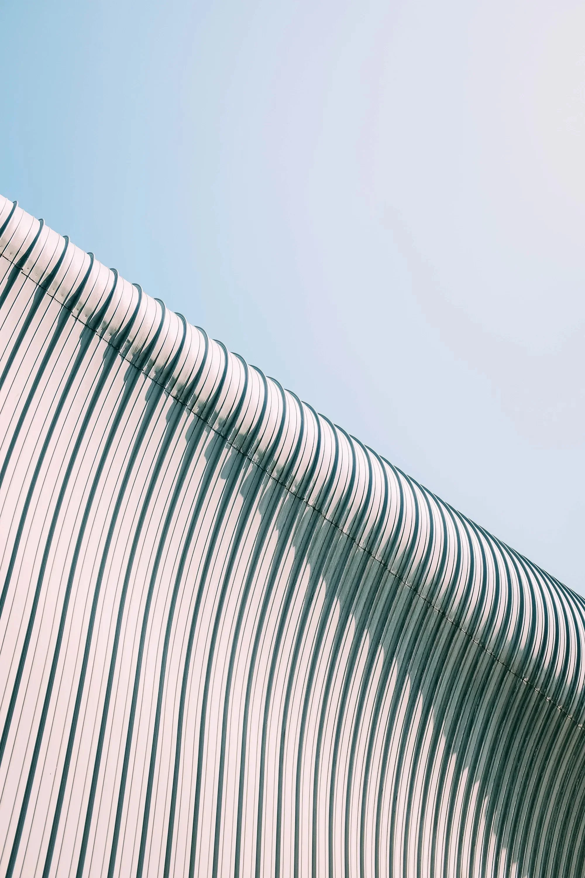 Close-up of a modern architectural building with white, curved, ribbed panels against a clear blue sky.