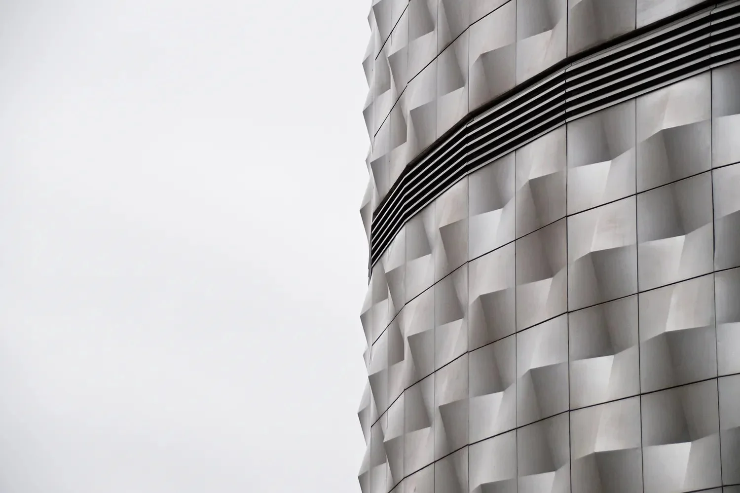 Close-up of a modern building's exterior featuring geometric, textured gray panels and horizontal black louvers.
