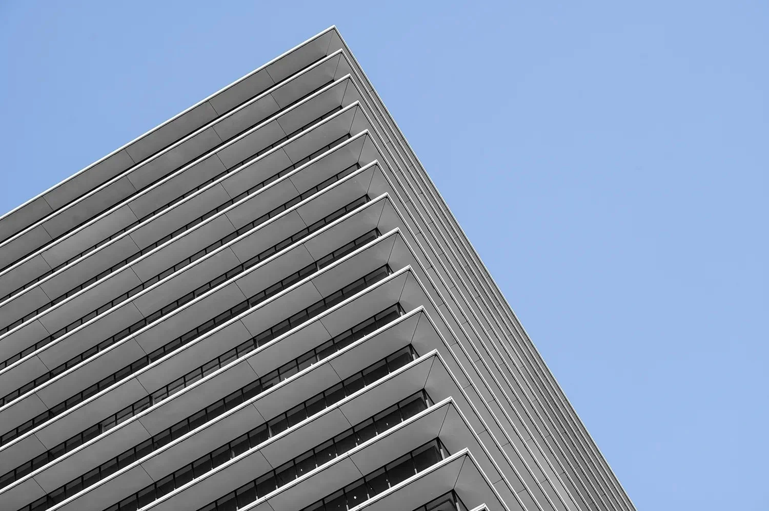 Low-angle view of a modern high-rise building with multiple balconies against a clear blue sky.