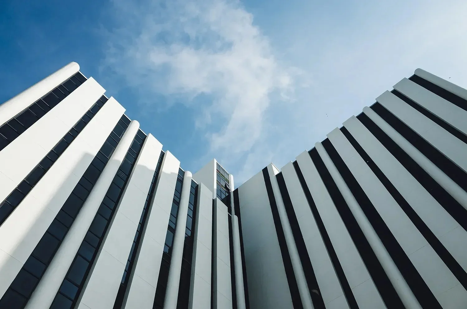 Low-angle view of a modern white high-rise building with black accents against a partly cloudy blue sky.