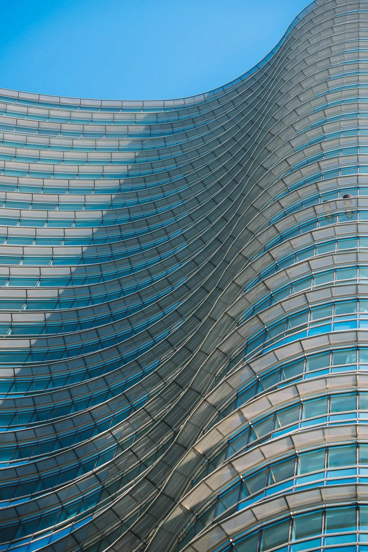 Modern building with curved glass facade and a clear blue sky.